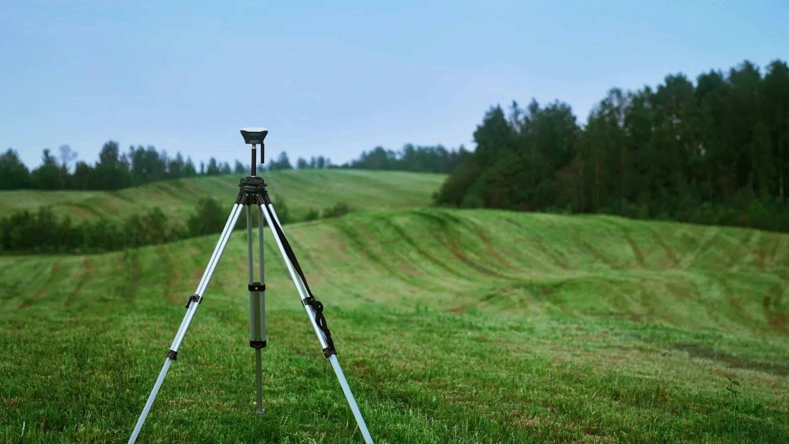 Receptor GNSS sobre trípode en un prado ondulado durante un levantamiento topográfico