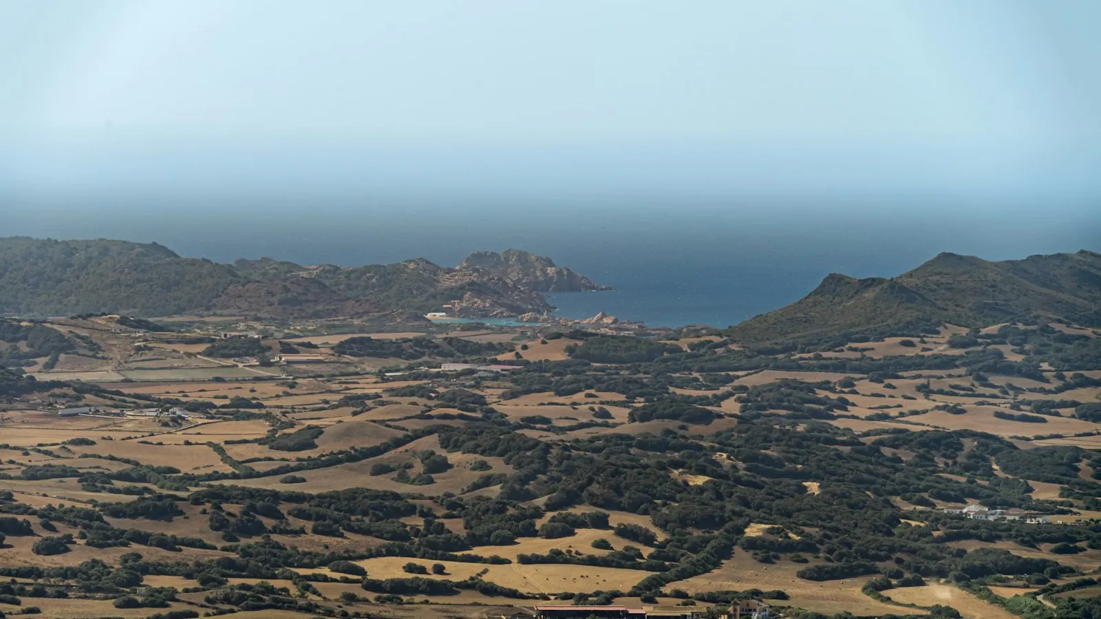 Paisaje rural de Menorca con campos, bosque bajo y la costa al fondo