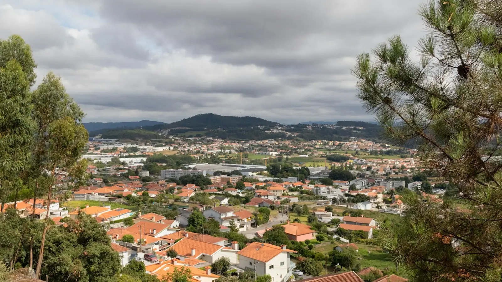 Vista de uma vila do Minho com telhados, arvoredo e colinas ao fundo